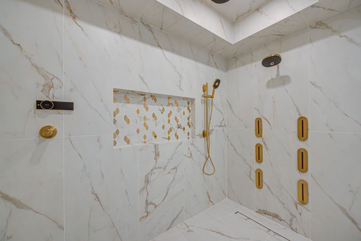 Elegant gold shower fixtures and patterned niche in luxury bath by Long Island Creative Contracting, Inc. in Port Jefferson, NY
