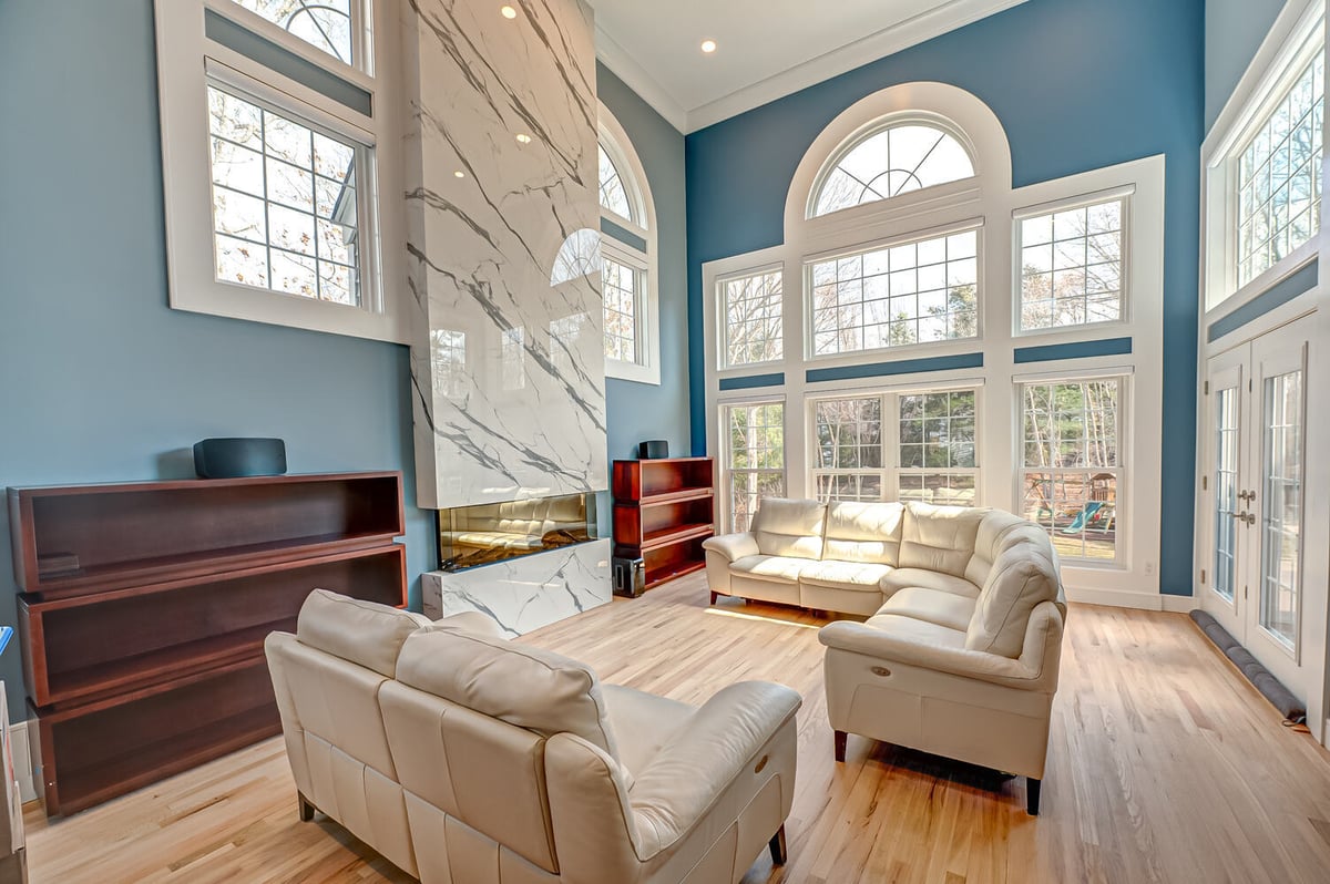Light-filled luxury living room with high ceilings and marble feature fireplace in Mount Sinai, NY home by Long Island Creative Contracting, Inc